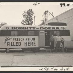 A man and woman stand outside of a trailer converted into a pharmacy