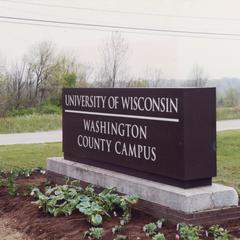 Campus entrance sign along University Drive with student gardening
