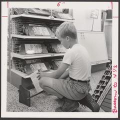 A young boy examines a book rack in a drugstore display