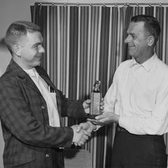 Unidentified photo of two men. One is handing an award to the other.