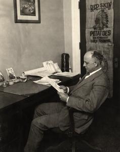 James G. Milward at desk, potato sack in background