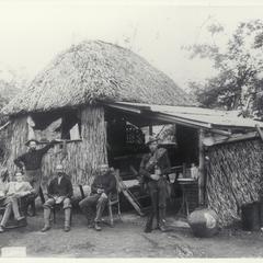 Five U.S. soldiers pose outside a thatched and tin-roofed hut, 1899