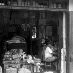 Chinese merchant inside shop selling suitcases, cloth