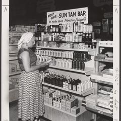 A woman selects suntan lotion from a drugstore display