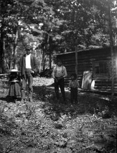 Unidentified man and children near cabin