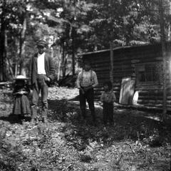 Unidentified man and children near cabin