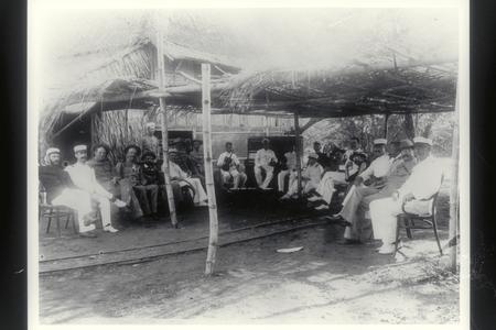 U.S. officers and men relax under a thatched awning to listen to Filipino musicians, 1899