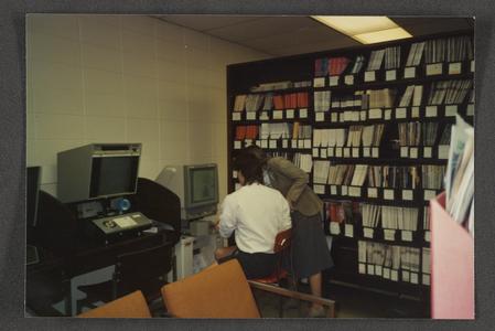 Student utilizing microfilm machine with help of librarian in library