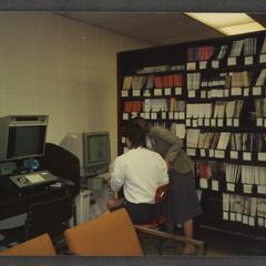 Student utilizing microfilm machine with help of librarian in library