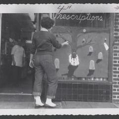 Teenager paints a drugstore window display with a ghostly scene for Halloween