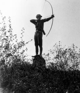 Aldo Leopold on stump with bow drawn