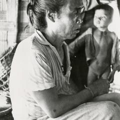 A White Lahu (Lahu Hpu) man is seated on the porch of his home in Houa Khong Province