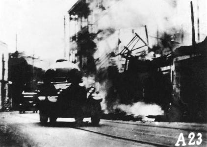 Japanese armored vehicles rolling along ruined city street.