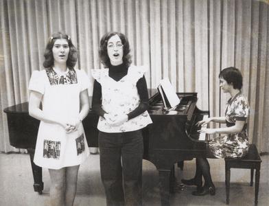 Two women singing accompanied by female pianist