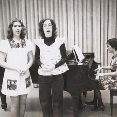 Two women singing accompanied by female pianist