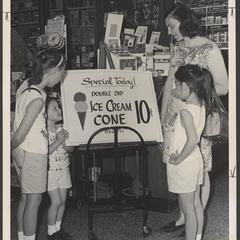 A mother and her daughters stand next to a sign promoting 10c ice cream cones