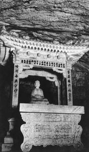 Buddha statue in a carved stone shrine inside a cave.