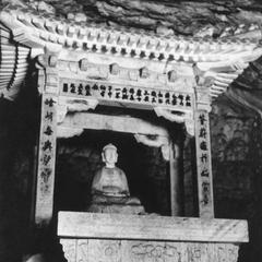 Buddha statue in a carved stone shrine inside a cave.