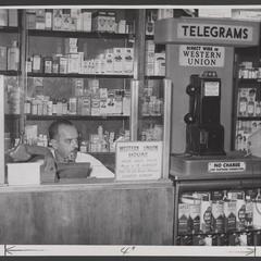 Man sits at a Western Union counter in a drugstore