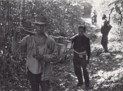 Villagers in the Houei Kong Cluster carry a generator along a trail in Attapu Province
