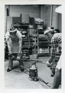 Two male students prepping to pour molten metal into a mold