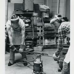 Two male students prepping to pour molten metal into a mold