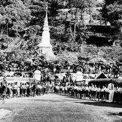 Townsfolk gather at base of Phu Si, opposite palace; schoolchildren with flowers line palace driveway