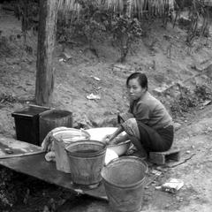 Lao woman washing dishes in ditch along road