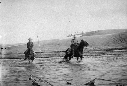 Postcard of men riding horses across river in Southwest