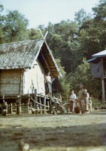 A Nyaheun village showing a house, villagers and background forest in Attapu Province
