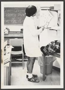 Student holding a copy of 'Ubiquitous' in a labcoat and shorts