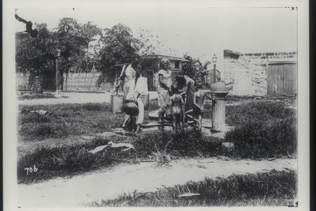 Filipino adults and children drinking and bathing at public fountain, early 1900s