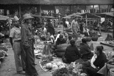 Soldiers looking over seated Lao women vegetable vendors