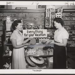 A saleswoman helps a customer select items at a drugstore vacation display