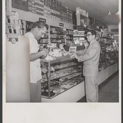 Pharmacist holds camera as man stands at a counter